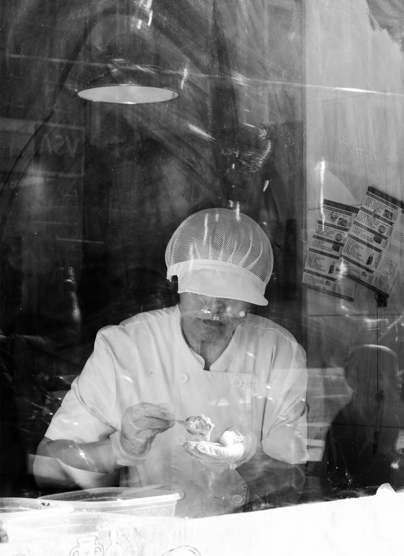 Baker in a shop window making dessert